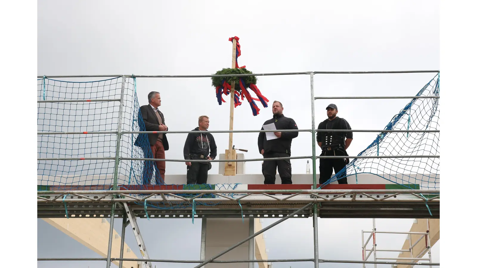 Der Richtkranz weht über der entstehenden Feuerwache Nord in Hohnhorst. Samtgemeindebürgermeister Mike Schmidt beim Ausbringen des Richtspruches mit Vertretern der beteiligten Handwerksfirmen. (Foto: Borchers, Bastian)