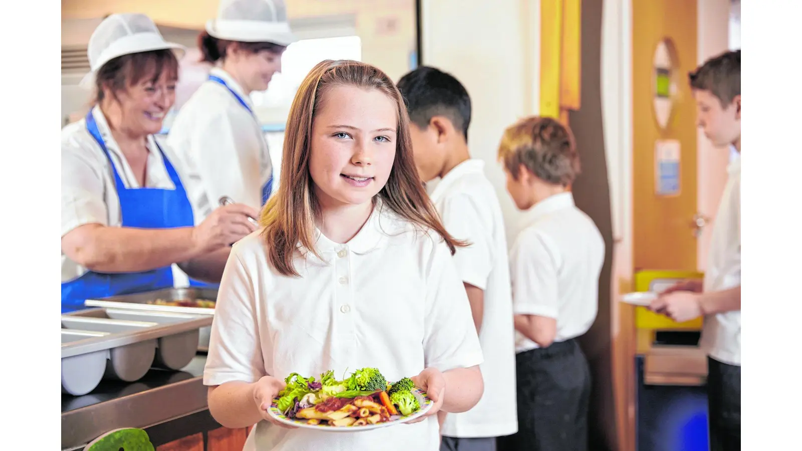 Girl holds a plate of food in school cafeteria, head turned (Foto: nh)